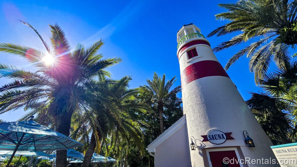 The white and red lighthouse sauna at Disney’s Old Key West resort is seen next to green palm trees under a sunny sky.