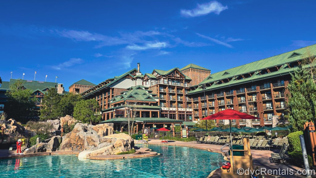 The Copper Creek Springs Pool is seen under a blue sky. The log cabin-style resort exterior can be seen in the background.