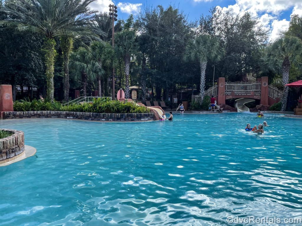 Guests enjoy swimming and the waterslides at the Samawati Springs Pool at Disney’s Animal Kingdom Villas Kidani Village under a blue sky.