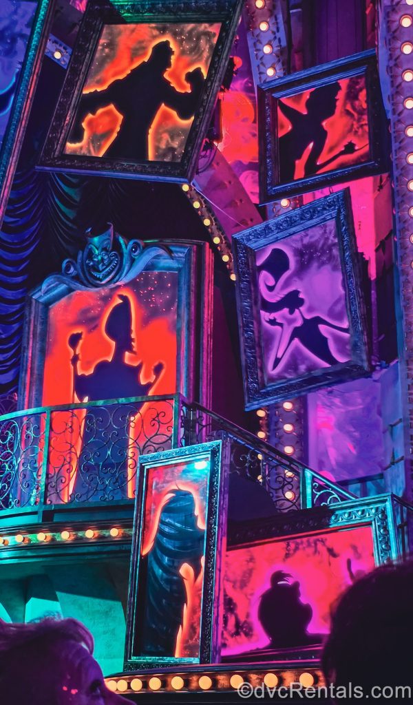 Silhouettes of Disney Villains such as Jafar, Yzma, and more are seen in the stage design of the Villains Unfairly Ever After show, lit with shades of red, purple, and green.