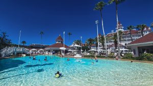 Guests enjoy a sunny day at the Beach Pool at Disney’s Grand Floridian Resort & Spa as the monorail glides past the resort in the background.