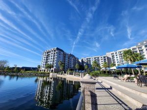 Guests sit at the umbrella-covered tables seen along the waterside at Disney’s Riviera Resort under a bright sunny sky.