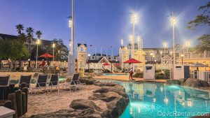Lounge chairs, sand, and a portion of the Stormalong Bay pool area is seen at Disney’s Beach Club Villas under a clear evening sky.