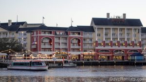 Two Friendship Boats sit docked in front of Disney’s BoardWalk Villas. The lights along the BoardWalk are lit as the sun begins to set over the resort’s colorful exterior.