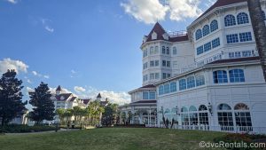 The landscaped grounds, white exterior walls and iconic red roof of Disney’s Grand Floridian Resort & Spa are seen on a sunny day.