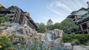 Little orange and yellow flowers pop in the landscaping outside Disney’s Wilderness Lodge, as seen under a hazy sky at twilight.
