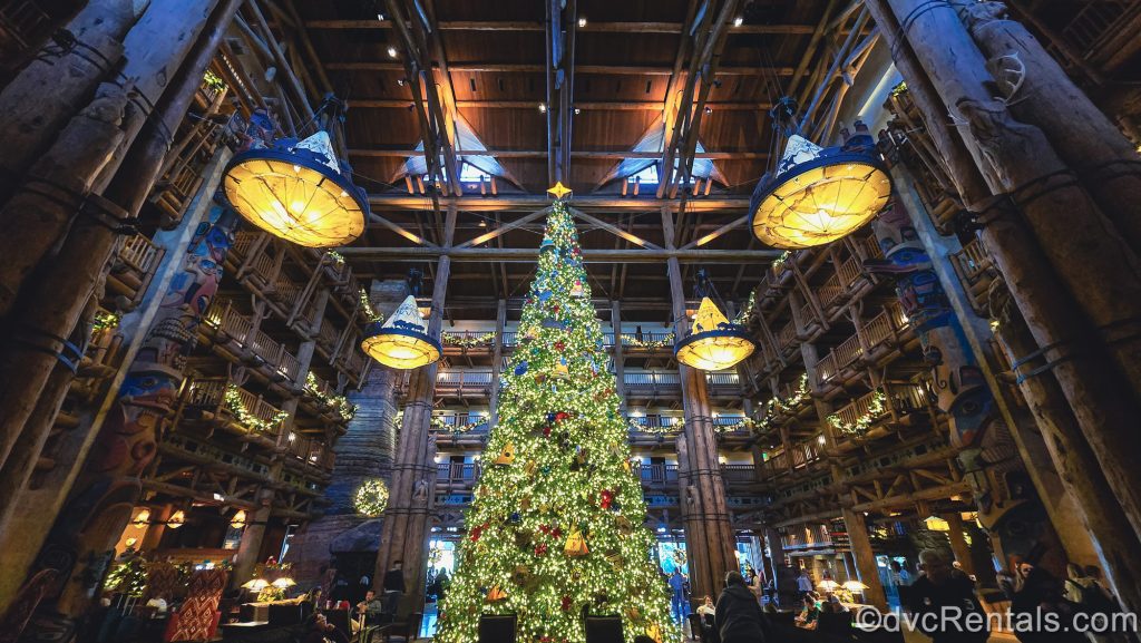 A very tall Christmas tree decorated with white lights and themed ornaments delights guests in the log cabin-style lobby of Disney’s Wilderness Lodge during the holiday season.