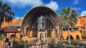 The exterior of Disney’s Animal Kingdom Villas Kidani Village is seen under a blue sky. The building is brown with multicolored accents inspired by African art.