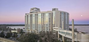 The circular exterior or Bay Lake Tower at Disney’s Contemporary Resort is seen from a high floor at sunset under a pink and purple sky.