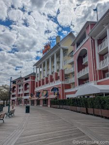 The colorful exterior of Disney’s BoardWalk Villas is seen under a blue sky as the boardwalk itself stretches out for guests to enjoy below.