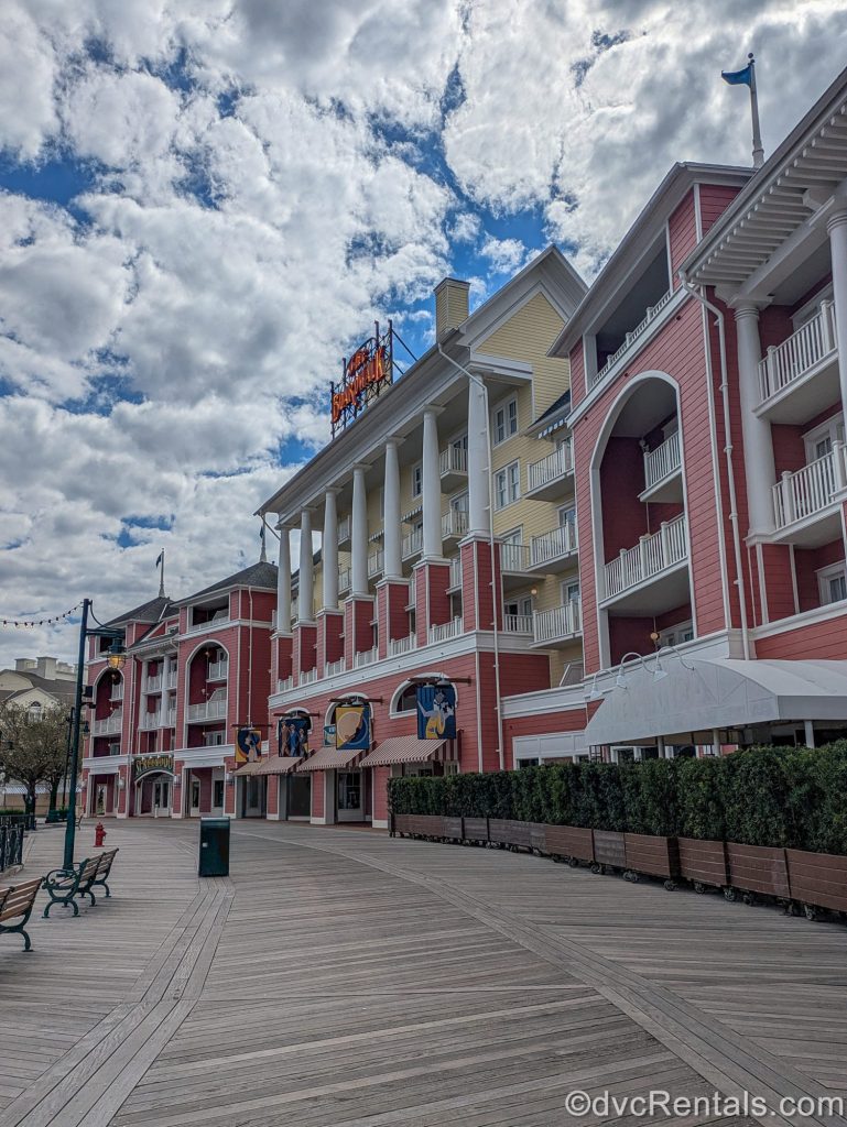 The colorful exterior of Disney’s BoardWalk Villas is seen under a blue sky as the boardwalk itself stretches out for guests to enjoy below.