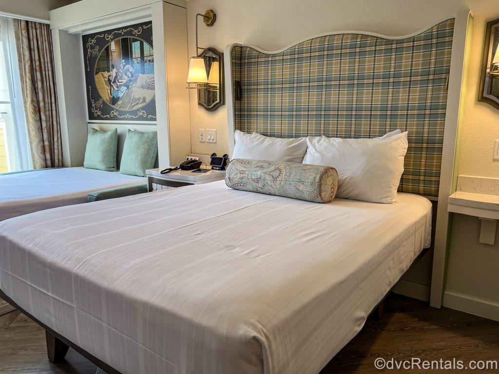 A Deluxe Studio at Disney’s BoardWalk Villas. The room is decorated with neutral tones, plaids and patterns, pops of green, and Disney inspired artwork and accents.