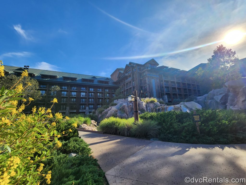 The log cabin-inspired exterior of Disney’s Wilderness Lodge is seen during golden hour under a blue sky as the resort’s landscaping is seen in the foreground