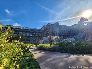 The log cabin-inspired exterior of Disney’s Wilderness Lodge is seen during golden hour under a blue sky as the resort’s landscaping is seen in the foreground