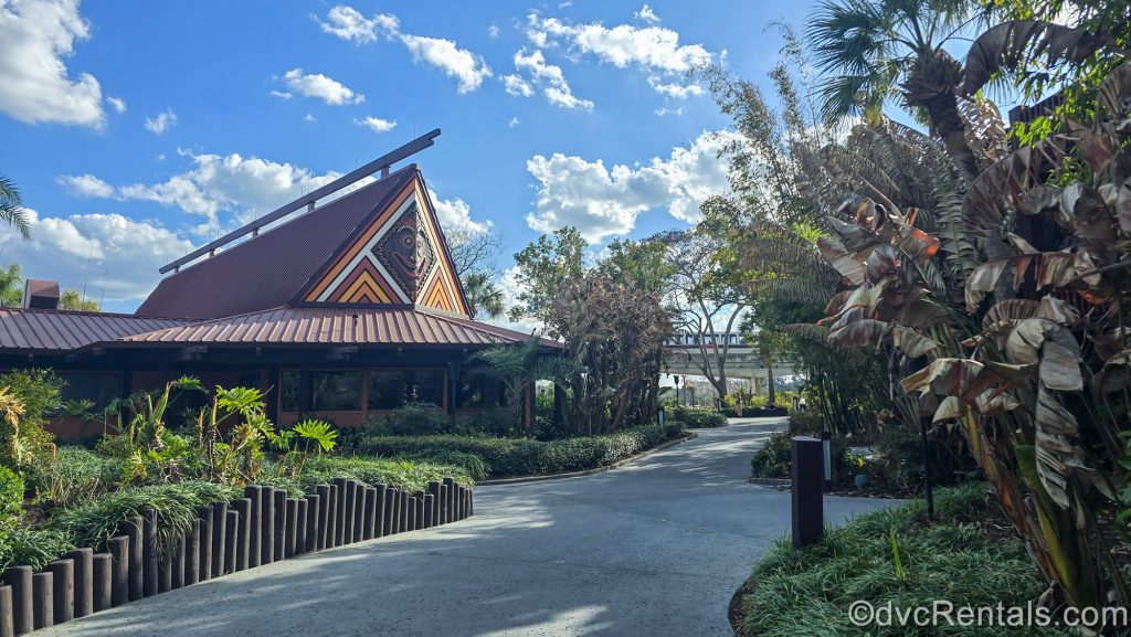 The dark brown exterior of a Longhouse and grounds landscaping at Disney’s Polynesian Villas & Bungalows. The monorail can be seen going by in the distance.