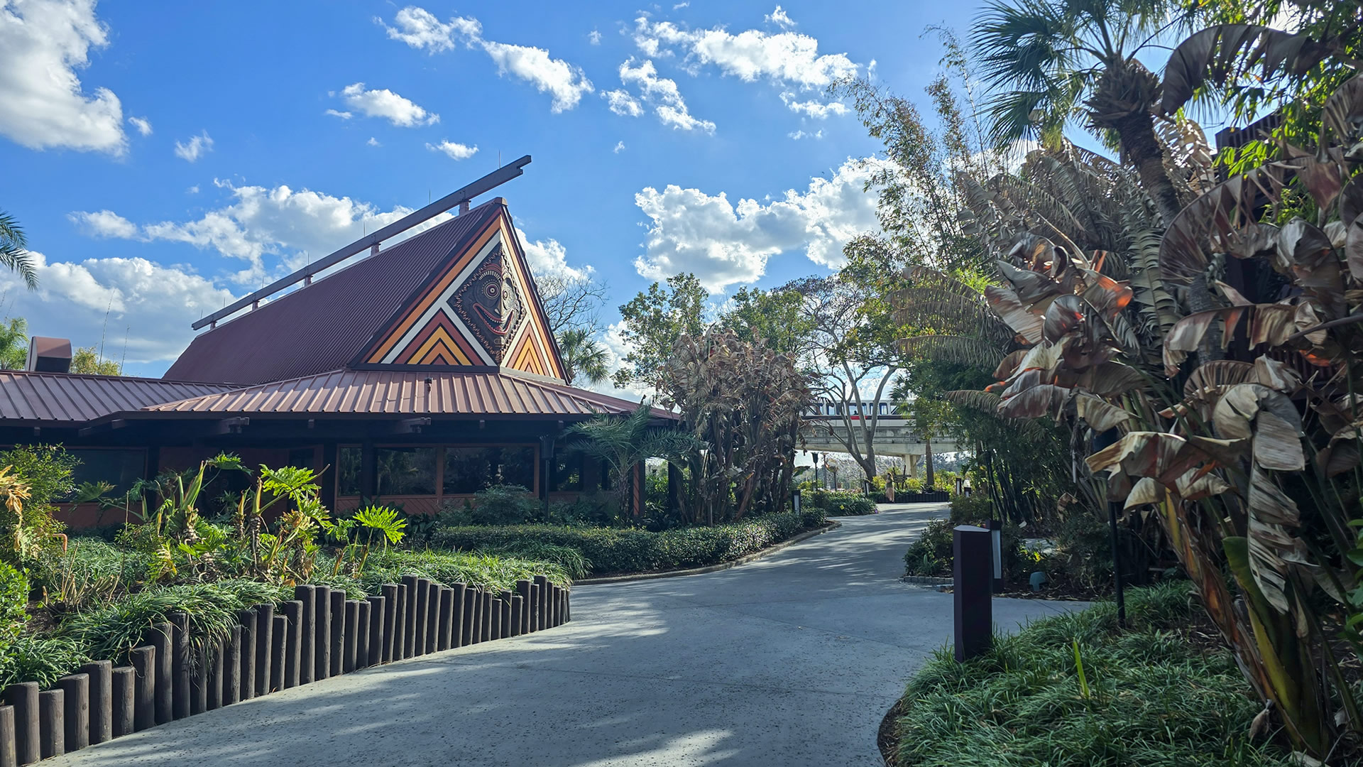 The dark brown exterior of a Longhouse and grounds landscaping at Disney’s Polynesian Villas & Bungalows. The monorail can be seen going by in the distance.