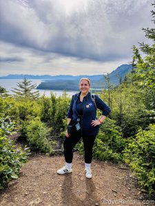 David’s Vacation Club Rentals team member Stacy R. poses along a hiking trail with the mountains and ocean in the distance.