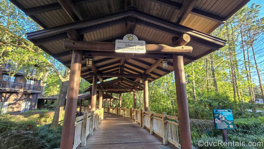 The covered wooden walkway leading to the Boulder Ridge Villas at Disney’s Wilderness Lodge is seen, with green trees and foliage surrounding it.
