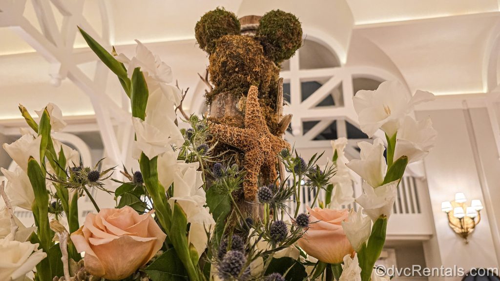 A floral display featuring white and pink flowers, a moss-covered hidden Mickey, and starfish is seen in the lobby of Disney’s Beach Club Villas.