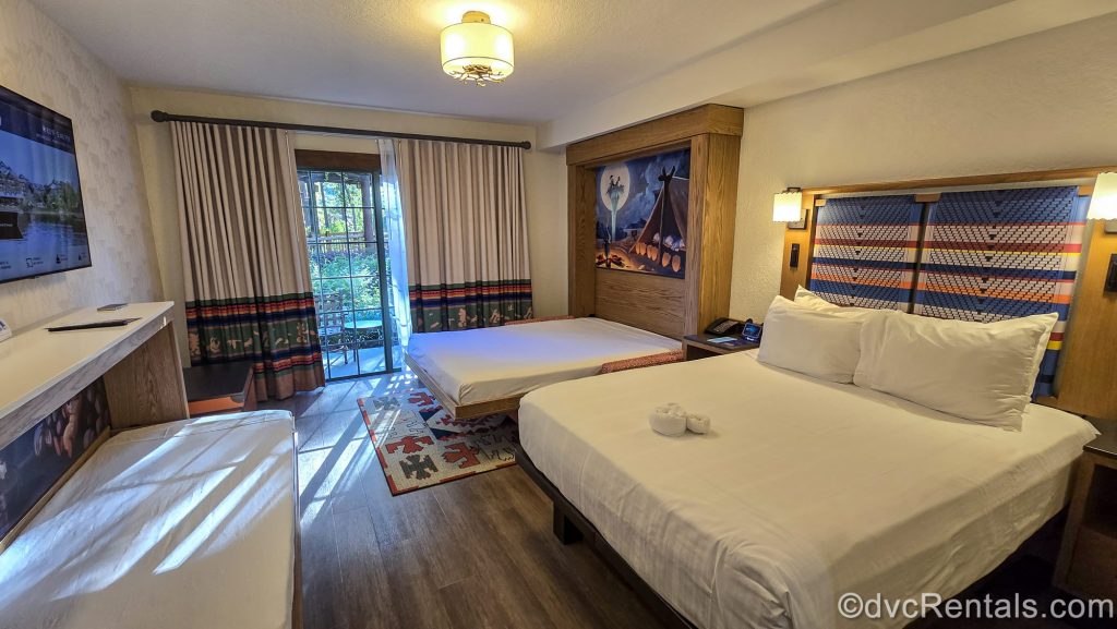 The queen size bed, pull-down Murphy Bed, and pull-down bunk-style bed are seen in a Deluxe Studio at the Boulder Ridge Villas at Disney’s Wilderness Lodge. The room is decorated with nature-inspired prints and neutral tones with pops of blue, orange, and green.
