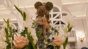 A floral display featuring white and pink flowers, a moss-covered hidden Mickey, and starfish is seen in the lobby of Disney’s Beach Club Villas.