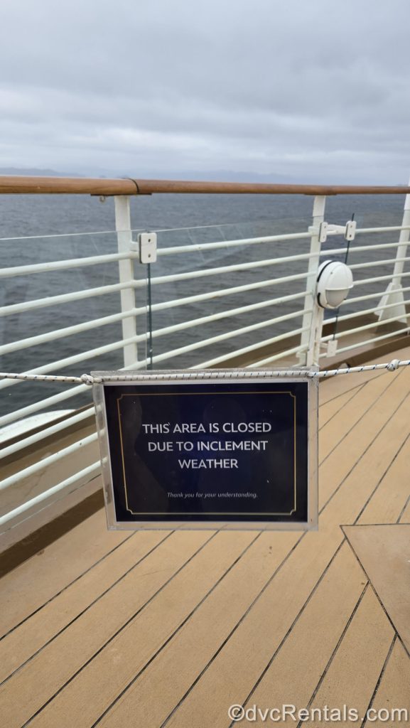 A blue sign reading “This area is closed due to inclement weather” is strung up on an outdoor deck of the Disney Magic as it sails through the Pacific.