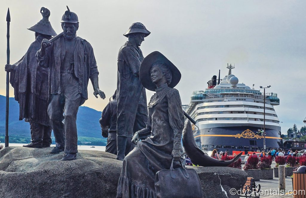 Statues of historical figures are seen with the Disney Magic cruise ship in the background while docked in port in Ketchikan, Alaska.