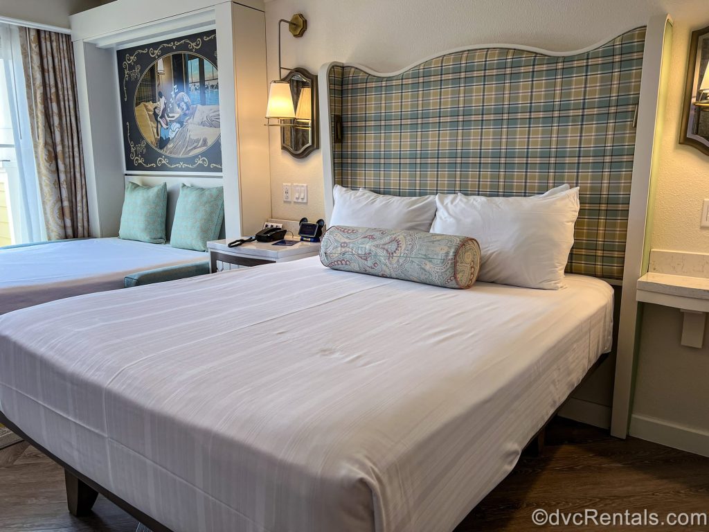 The queen bed and Murphy bed in a Studio at Disney’s BoardWalk Villas. The room features pastels, paisley, and plaid prints, along with Disney characters in the artwork accents.