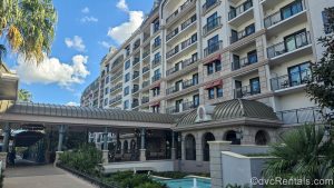 The European-inspired front entrance and building exterior of Disney’s Riviera Resort is seen under a blue sky filled with fluffy, white clouds.