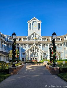 Holiday garlands decorated with multicolored ornaments decorate the lampposts outside Disney’s Beach Club Villas under a bright blue sky.
