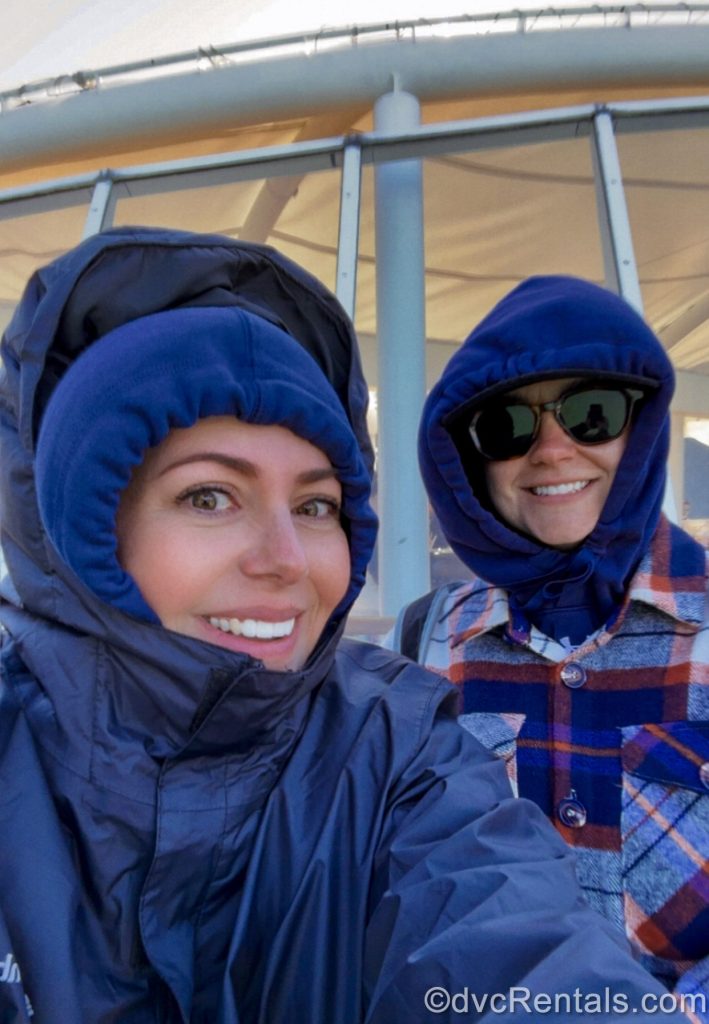 David’s Vacation Club Rentals team members Stacy R. and Olivia smile for the camera in their coats and jackets as they enjoy glacier viewing on the Disney Magic.