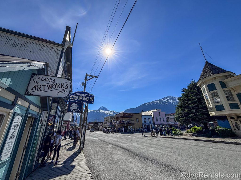 Bright sunshine pours over the mountains and town of Skagway, Alaska as visitors explore the shops and restaurants in port.