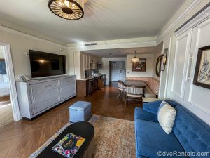 The living room, dining area, and kitchen in a One Bedroom Villa at Disney’s Riviera Resort. The room is decorated with pops of gemstone colors and Disney artwork inspired by classic European works.