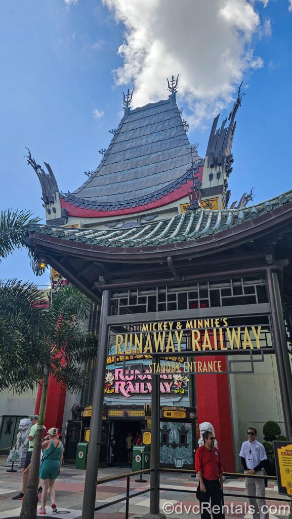 The standby queue entry into Mickey & Minnie’s Runaway Railway is seen outside the theater building under a bright, sunny sky.