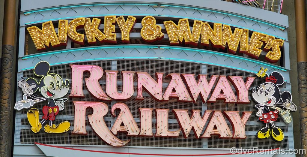 Neon lights displaying the attraction name “Mickey & Minnie’s Runaway Railway” along with depictions of Mickey and Minnie Mouse. The wording is in gold and pink.