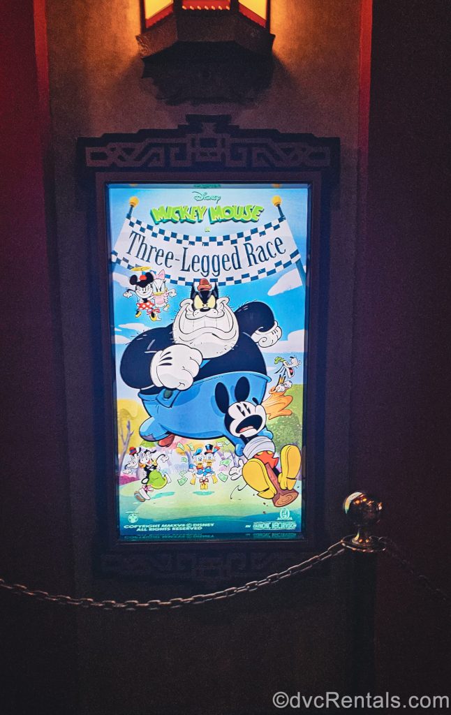 A poster depicting a scene from the Mickey Mouse Short “Three-Legged Race” is seen illuminated in a frame in the queue line for Mickey & Minnie’s Runaway Railway.