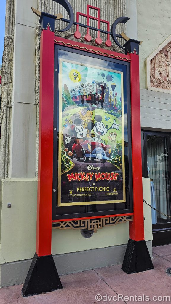A posted depicting a scene from the Mickey Mouse Short “Perfect Picnic” from the attraction is featured in a large red frame outside Mickey & Minnie’s Runaway Railway at Disney’s Hollywood Studios.