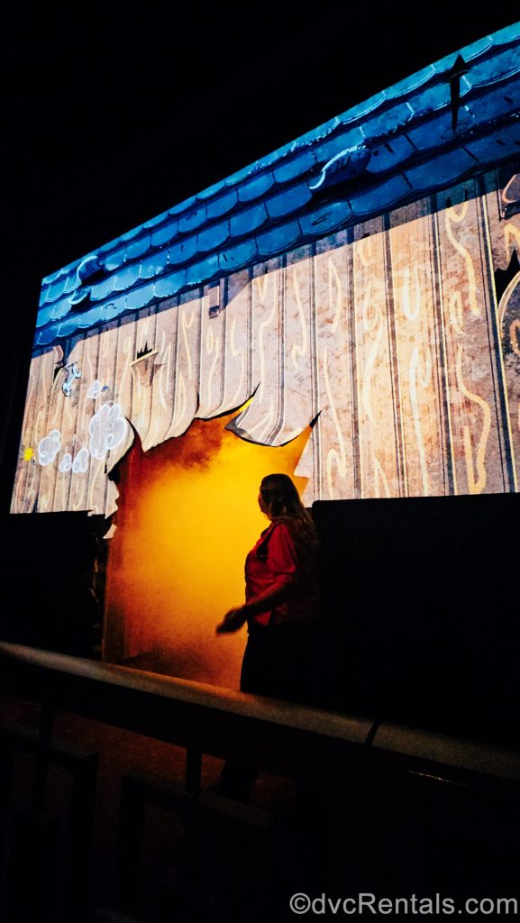 A Disney Cast Member interacts with the video pre-show segment of Mickey & Minnie’s Runaway Railway, where it looks as though a large hole has been blow in the theater’s screen.