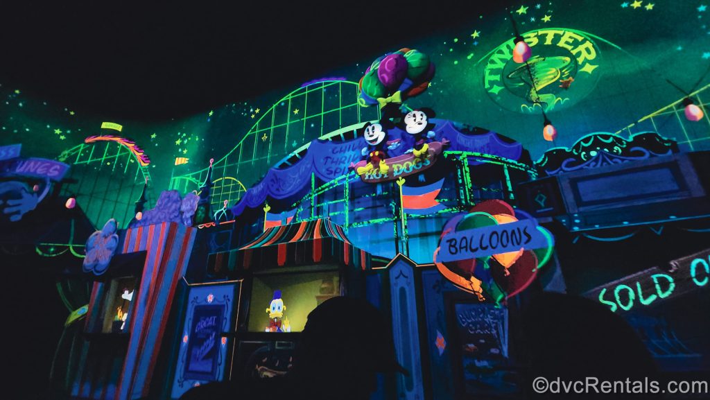 Guests ride through a scene where Mickey and Minnie Mouse float over a carnival as they hold onto a bunch of brightly-colored balloons.