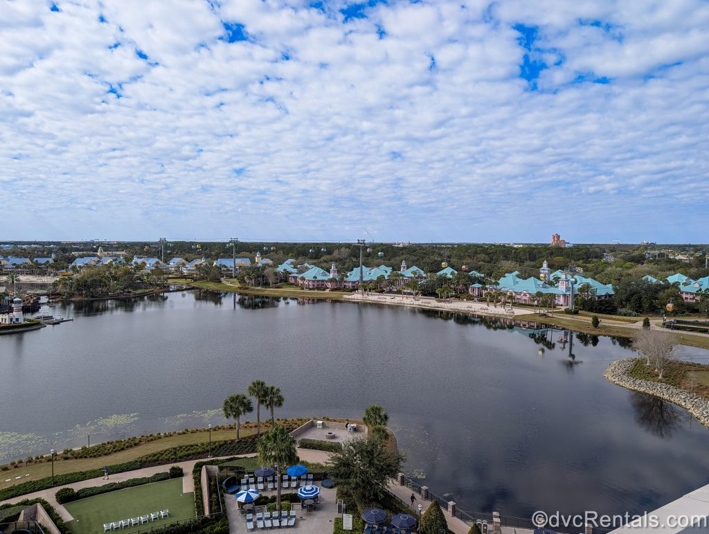 The grounds of Disney’s Caribbean Beach Resort and the Disney Skyliner system are seen from the outdoor terrace atop Disney’s Riviera Resort under a hazy blue sky.