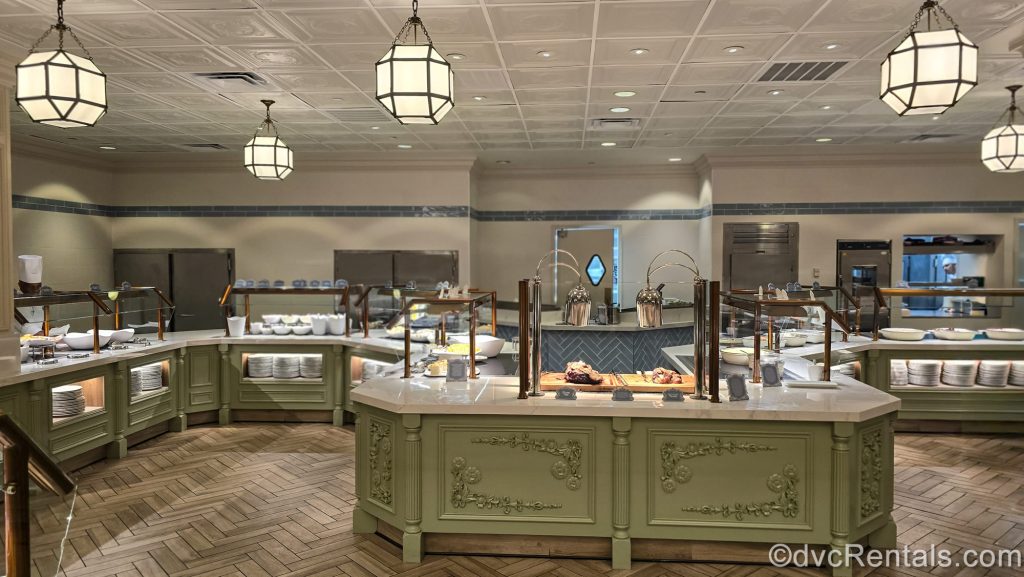 The buffet at 1900 Park Fare at Disney’s Grand Floridian Resort & Spa. Various foods served in white dishes as well as carving stations can be seen on the green and white counters.