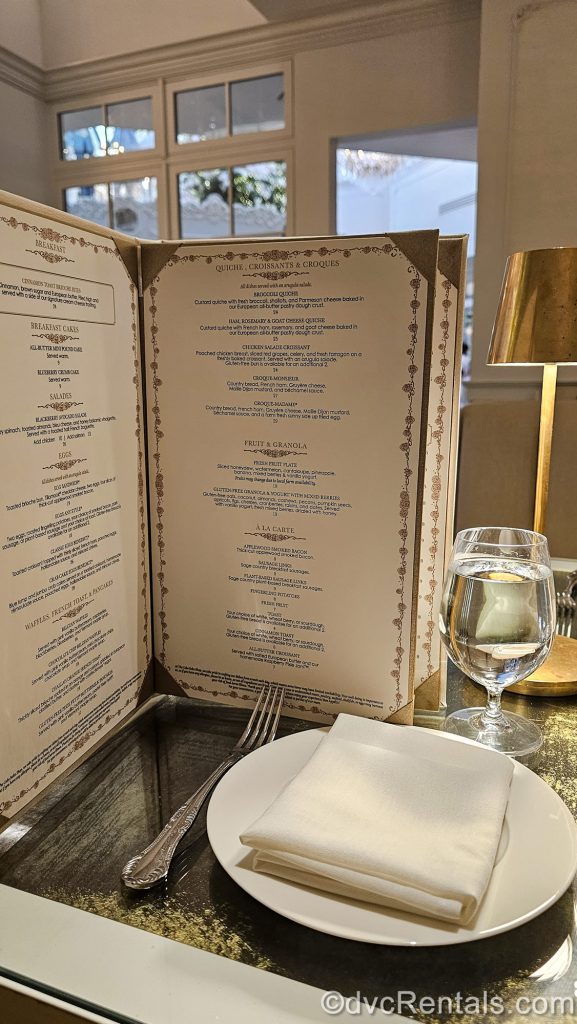 A breakfast menu and place setting with gold accents are seen on the table top at the Cake Bake Shop Restaurant by Gwendolyn Rogers at Disney’s BoardWalk Villas.