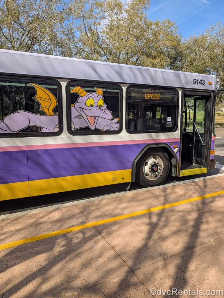 A Walt Disney World Transportation bus decorated with character Figment pulls up to take guests from Disney’s Saratoga Springs Resort & Spa to EPCOT.