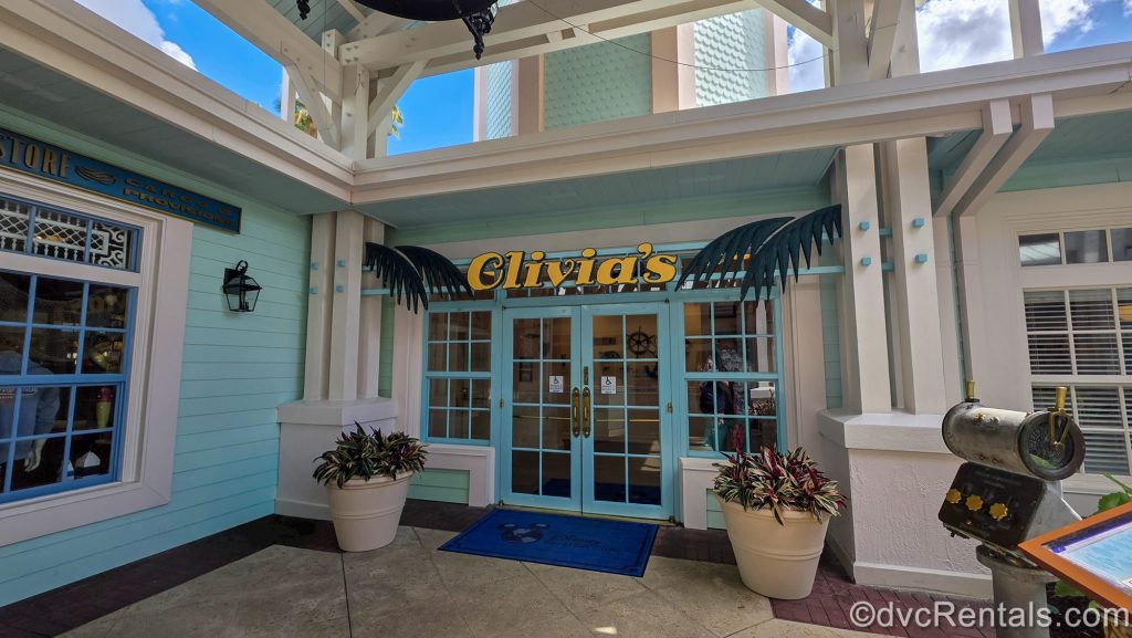 The entry doorway into Olivia’s Café at Disney’s Old Key West Resort. The exterior is painted in tones of turquoise and white, with dark green palm leaves, and the word “Olivia’s” in a golden yellow.