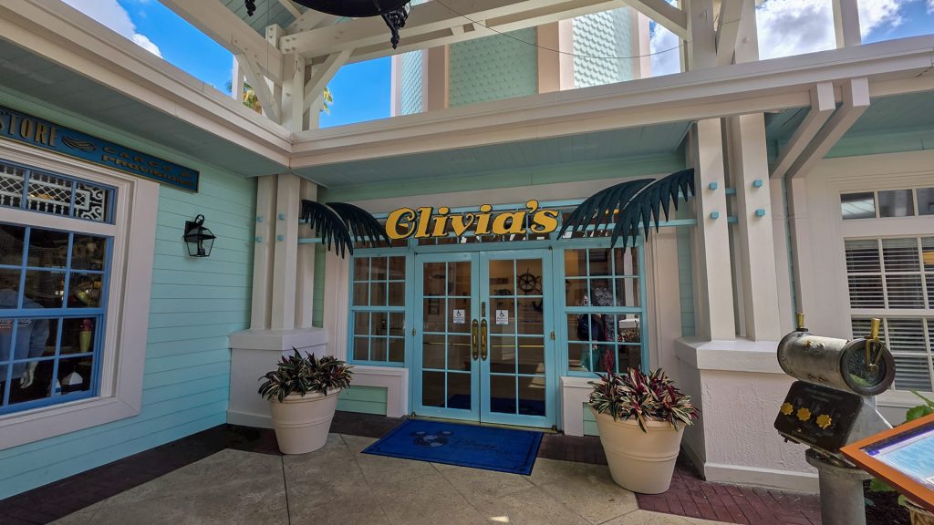 The entry doorway into Olivia’s Café at Disney’s Old Key West Resort. The exterior is painted in tones of turquoise and white, with dark green palm leaves, and the word “Olivia’s” in a golden yellow.